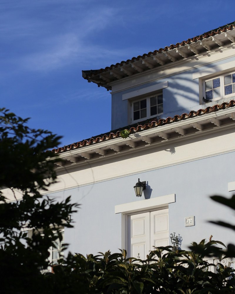 Fachada de una vivienda unifamiliar con tejado de teja y contraventanas blancas, rodeada de vegetación
